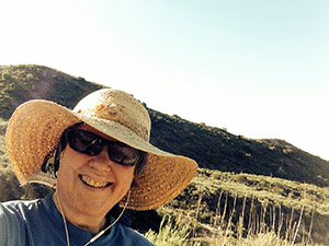 Laurie smiling in her straw hat on a sunny day on the trail in the foothills.