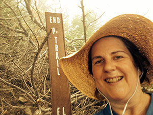 Laurie stands by the end of trail marker.