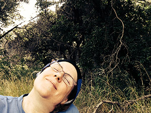 Laurie rests with her eyes shut under the tree at the trail head