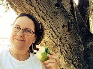 Close up by an oak tree of Laurie eating a green apple.