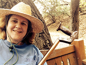Laurie with a cane on a bench under a tree.