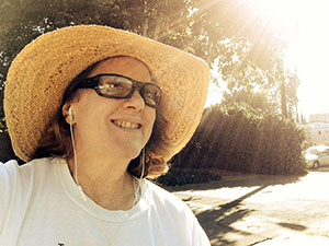 Laurie smiling in her straw hat with the sun shining down.