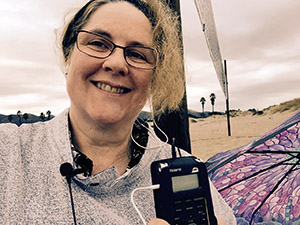 Laurie holds her recorder up by her face on a stormy day on the beach