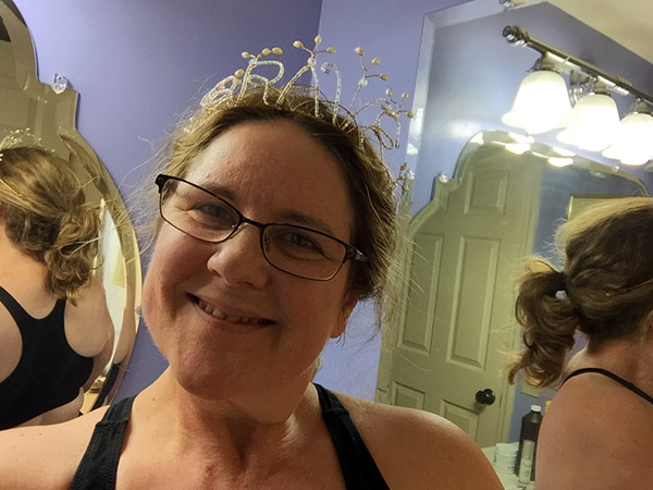 Laurie looking in the bathroom mirror while wearing a tiara that says 'BRAVE'.