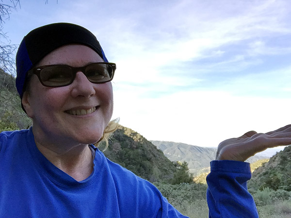 Laurie indicates the view of the valley below the mountain trail with an open hand gesture