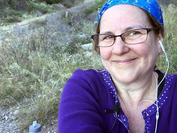 Laurie in blue scarf smiles against the wild grasses on the trail.