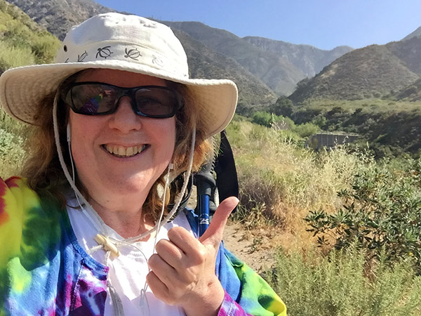 Laurie on the hiking trail on a sunny day giving thumbs up.