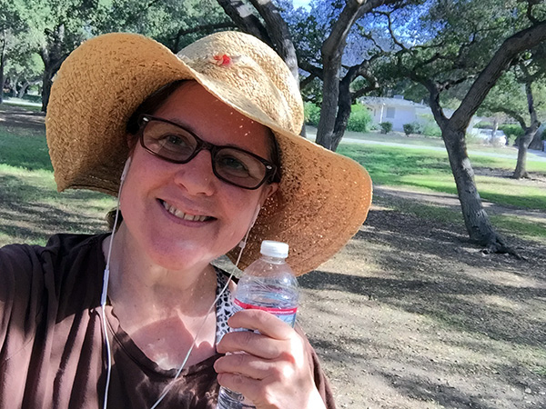 Laurie at the park wearing a straw sunhat and holding a water bottle