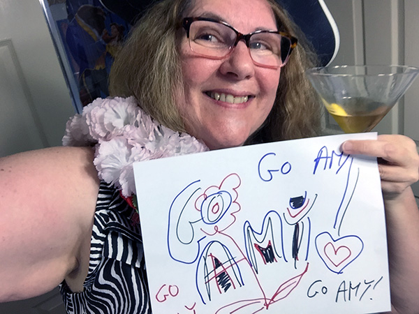 Laurie dressed up holding a sign that says Go Amy!