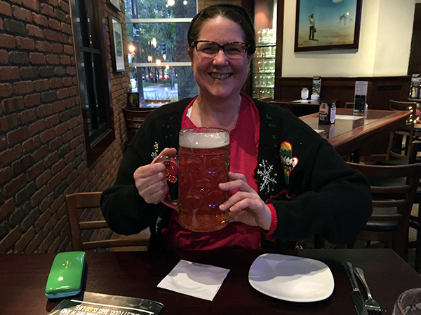 Laurie holding a monster size beer while wearing a holiday sweater