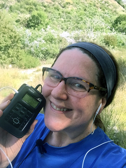 Laurie holds up her Roland Recorder and smiles into the camera while hiking