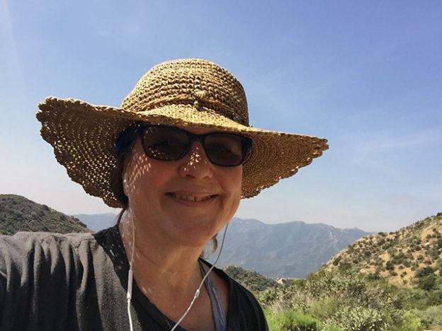 Laurie in her straw hat and sunglasses grins along the trail