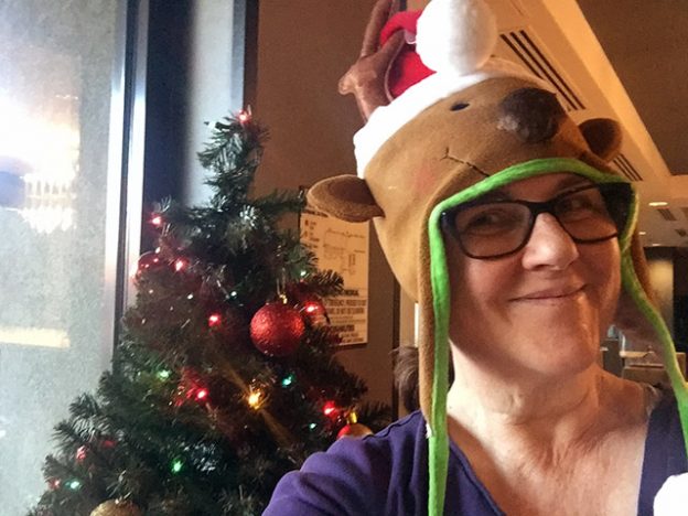 Laurie in front of a Christmas tree wearing a hat shaped like a reindeer