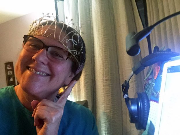 Laurie wearing a tiara that spells out the word BRAVE while smiling before her studio mic.