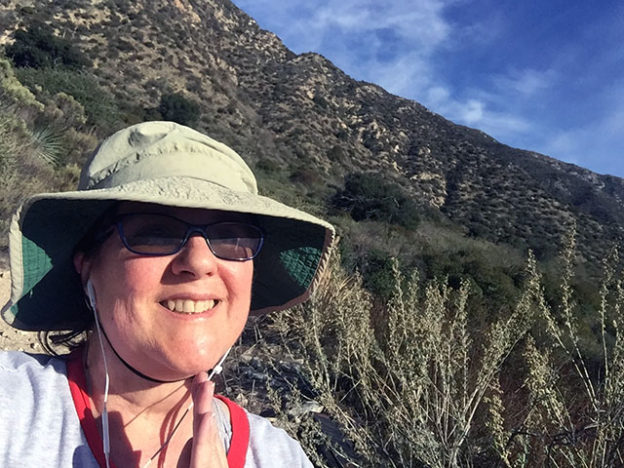 Laurie in hiking hat smiling against the mountain